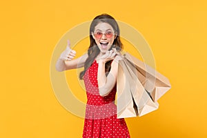 Excited young brunette woman girl in red summer dress, eyeglasses posing isolated on yellow wall background. People