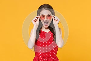 Excited young brunette woman girl in red summer dress, eyeglasses posing isolated on yellow wall background studio