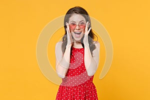 Excited young brunette woman girl in red summer dress, eyeglasses posing isolated on yellow wall background studio