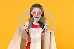 Excited young brunette woman girl in red summer dress, eyeglasses posing isolated on yellow wall background studio