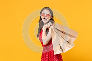 Excited young brunette woman girl in red summer dress, eyeglasses posing isolated on yellow wall background studio