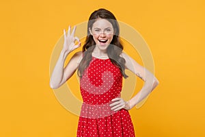 Excited young brunette woman girl in red summer dress posing  on yellow wall background studio portrait. People