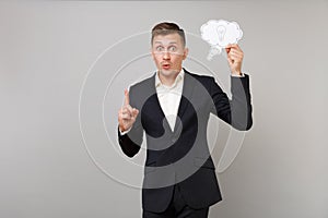 Excited young business man in suit holding say cloud with lightbulb, index finger up with great new idea isolated on