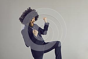 Excited young businessman with crazy funny hairstyle dancing on gray studio background