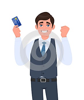 Excited young businessman showing credit, debit card. Man making or gesturing raised hand fist. Successful person in waistcoat.