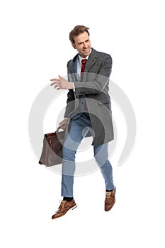 Excited young businessman with suitcase looking to side and leaping up