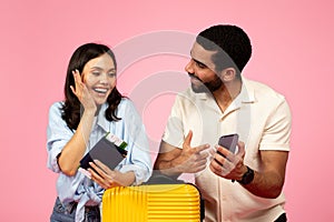 Excited young couple booking tickets online, pink background