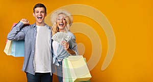 Excited Young Couple Holding Paper Bags And Bunch Of Dollars