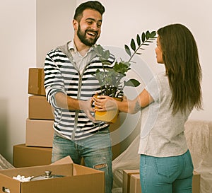 Excited young couple moving home standing close together with plants in their hands.