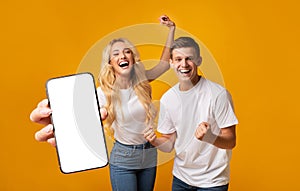 Excited Young Couple Showing Big Smartphone With White Screen And Celebrating Success