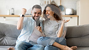 Excited young couple triumph reading news on cell