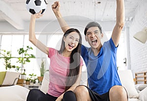 Excited Young couple watching tv and  raising hands to celebrating the victory