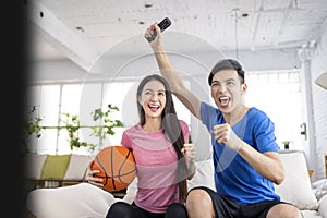 Excited Young couple watching tv and  raising hands to celebrating the victory