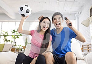 Excited Young couple watching tv and  raising hands to celebrating the victory