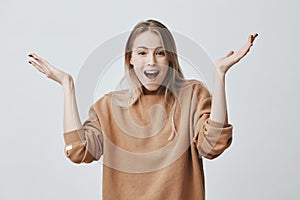 Excited young female with blonde hair exclaiming, looking at camera in amazement with opened mouth, clapping hands, glad