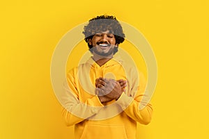 Excited young indian man holding hands on chest over heart