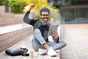 Excited young indian man using digital tablet on the street