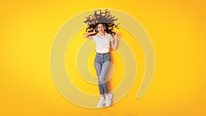 Excited Young Lady Listens Music With Headphones On Yellow Background