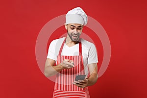 Excited young male chef cook or baker man in striped apron toque chefs hat isolated on red background. Cooking food