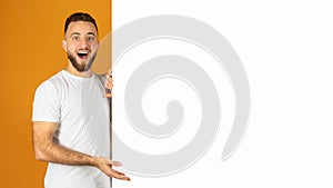 Excited young man with a beard joyfully peeks out from behind a blank white banner