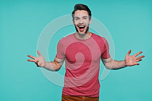 Excited young man in casual clothing looking at camera and keeping arms outstretched