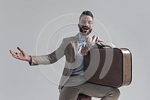 Excited young man holding arm on suitcase and presenting to side