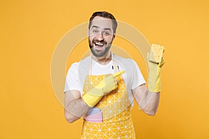 Excited young man househusband in apron rubber gloves doing housework isolated on yellow wall background studio portrait