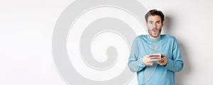 Excited young man making wish on birthday cake with lit candle, celebrating bday, standing on white background