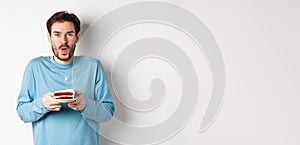 Excited young man making wish on birthday cake with lit candle, celebrating bday, standing on white background