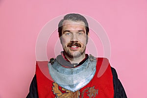 One young happy man, medieval warrior or knight wearing wearing armor clothing posing isolated over pink background