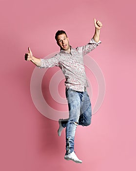 Excited young man in popular shirt jumping celebrating success pointing fingers thumbs up