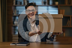 Excited young man sitting at workdesk, holding delivery box