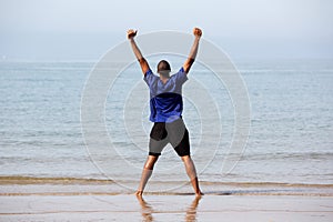 Excited young man standing on beach with arms outstretched