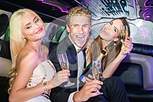 Excited young man with women holding champagne flutes in limousine during party