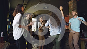 Excited young men and women coworkers are dancing and doing high-five celebrating victory at work. Office fun, corporate