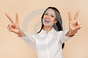 Excited young modern business woman showing peace gesture over beige background. Success and winner concept.