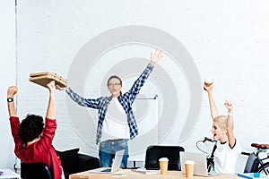 excited young start up team raising hands and looking at pizza boxes