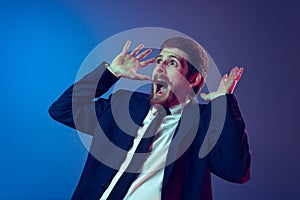 Excited young stylish man in business suit shouting  on dark blue studio background. Concept of human emotions