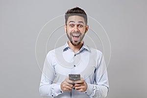 Excited young unshaven business man in light shirt posing isolated on grey background in studio. Achievement career