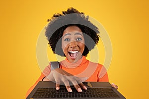 Excited young woman with an afro hairstyle exuberantly typing on a laptop