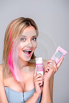 excited young woman with colored bob cut holding hair care supplies and looking at camera