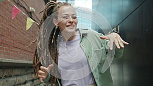 Excited young woman with creative dreads dancing outdoors smiling enjoying music and leisure time