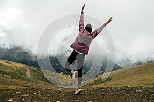 Excited young woman enjoying the view high up in cloudy mountains