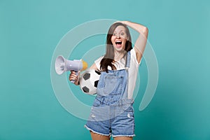 Excited young woman football fan support favorite team with soccer ball, megaphone putting hand on head isolated on blue