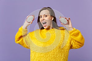 Excited young woman in fur sweater keeping mouth open holding halfs of pitahaya, dragon fruit isolated on violet pastel