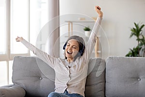 Excited young woman in headphones enjoying favorite music at home