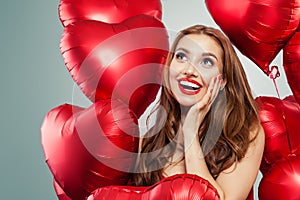 Excited young woman holding balloons red heart. Surprised girl with red lips makeup, long curly hair and cute smile