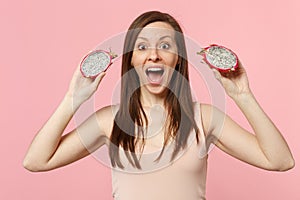 Excited young woman keeping mouth open holding fresh ripe pitahaya, dragon fruit isolated on pink pastel wall background