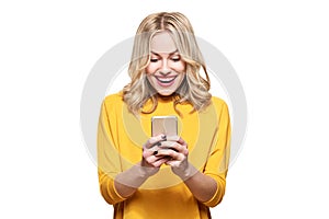 Excited young woman looking at her mobile phone smiling. Woman reading text message on her phone, isolated over white.