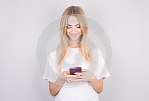 Excited young woman looking at her mobile phone smiling. Woman reading text message on her phone  isolated over white background